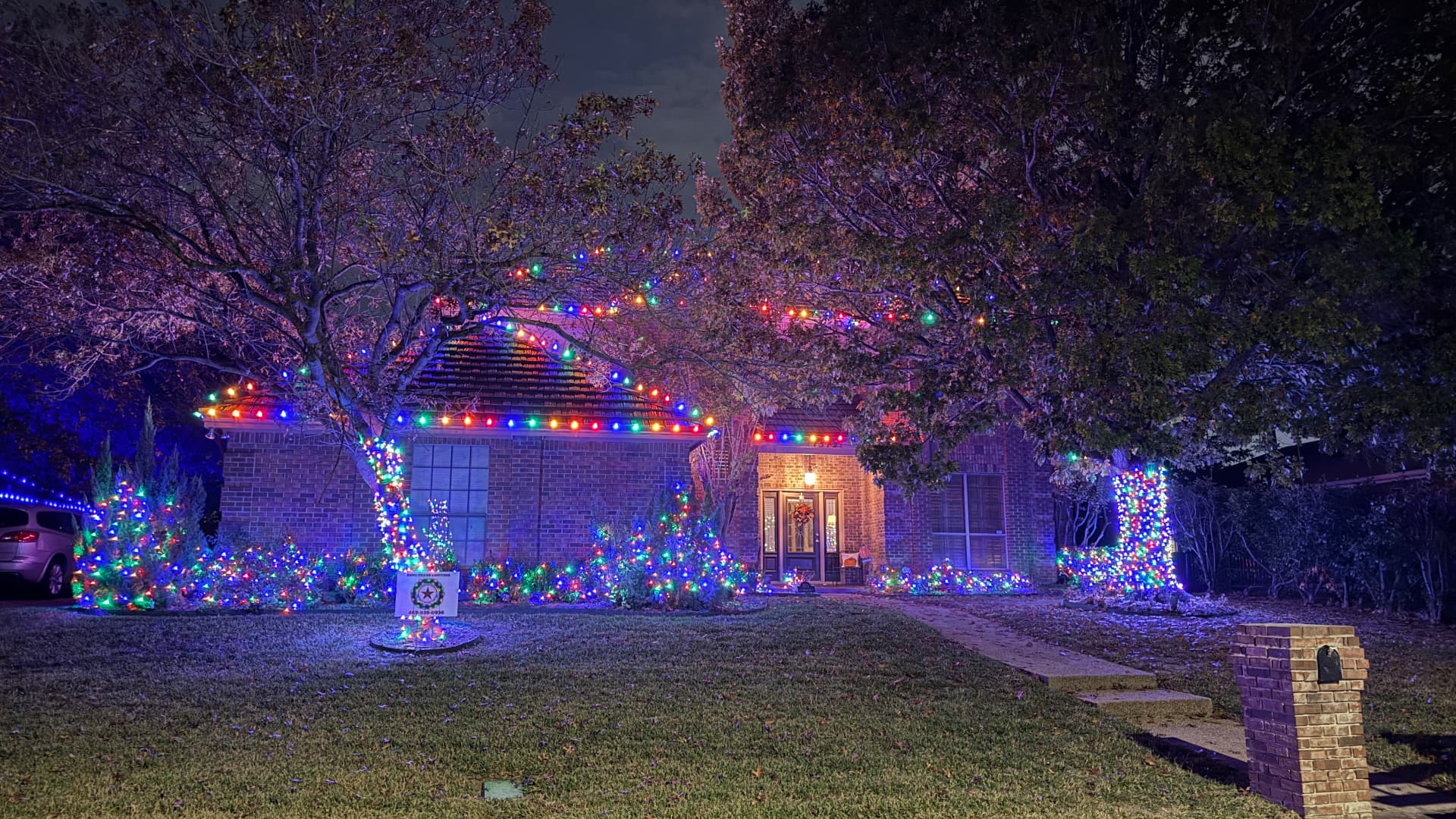 Full-color multicolor Christmas lights on a home's roofline, trees, and landscaping