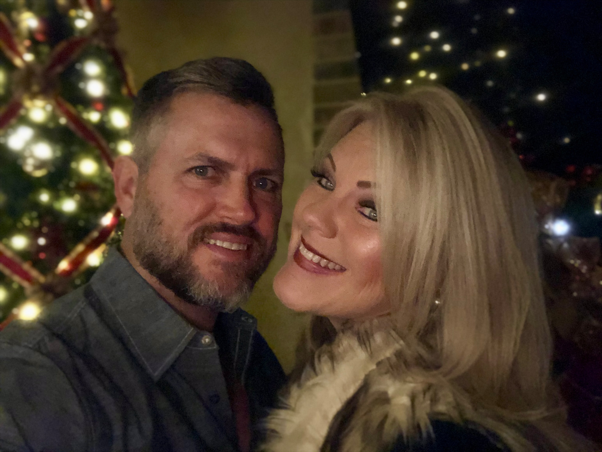 Craig and his wife smiling together beside a decorated Christmas tree